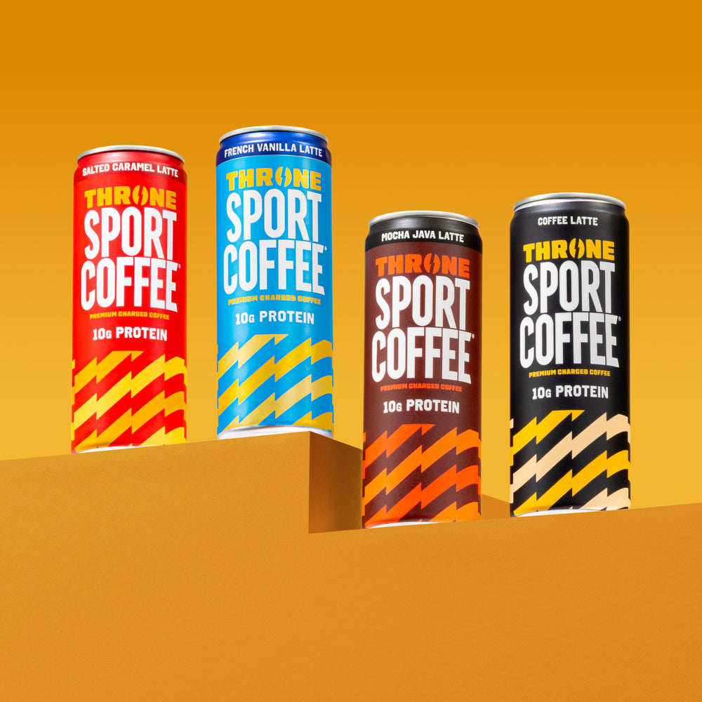Four Throne Sport Coffee cans—including Coffee Latte, Salted Caramel, French Vanilla Latte, and Mocha Java Latte—stand on a yellow-orange background and platform, each boldly labeled with 10g Protein and featuring vibrant designs. This lactose free protein coffee lineup is crafted for those seeking delicious sport coffee without compromise.