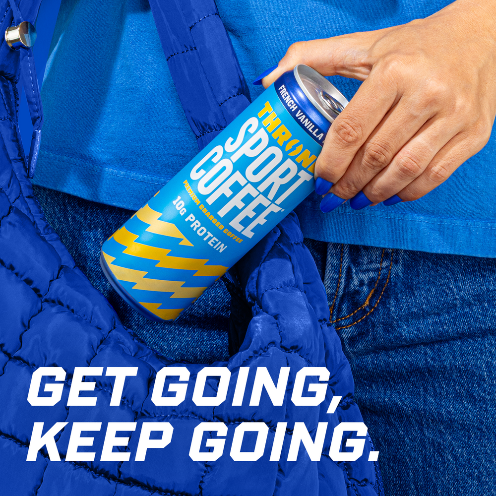 A hand holds a can of French Vanilla Latte high protein coffee near a blue quilted bag. Text on the image reads, GET GOING, KEEP GOING. The person, dressed in blue clothing and denim jeans, is ready to enjoy their lactose free boost.